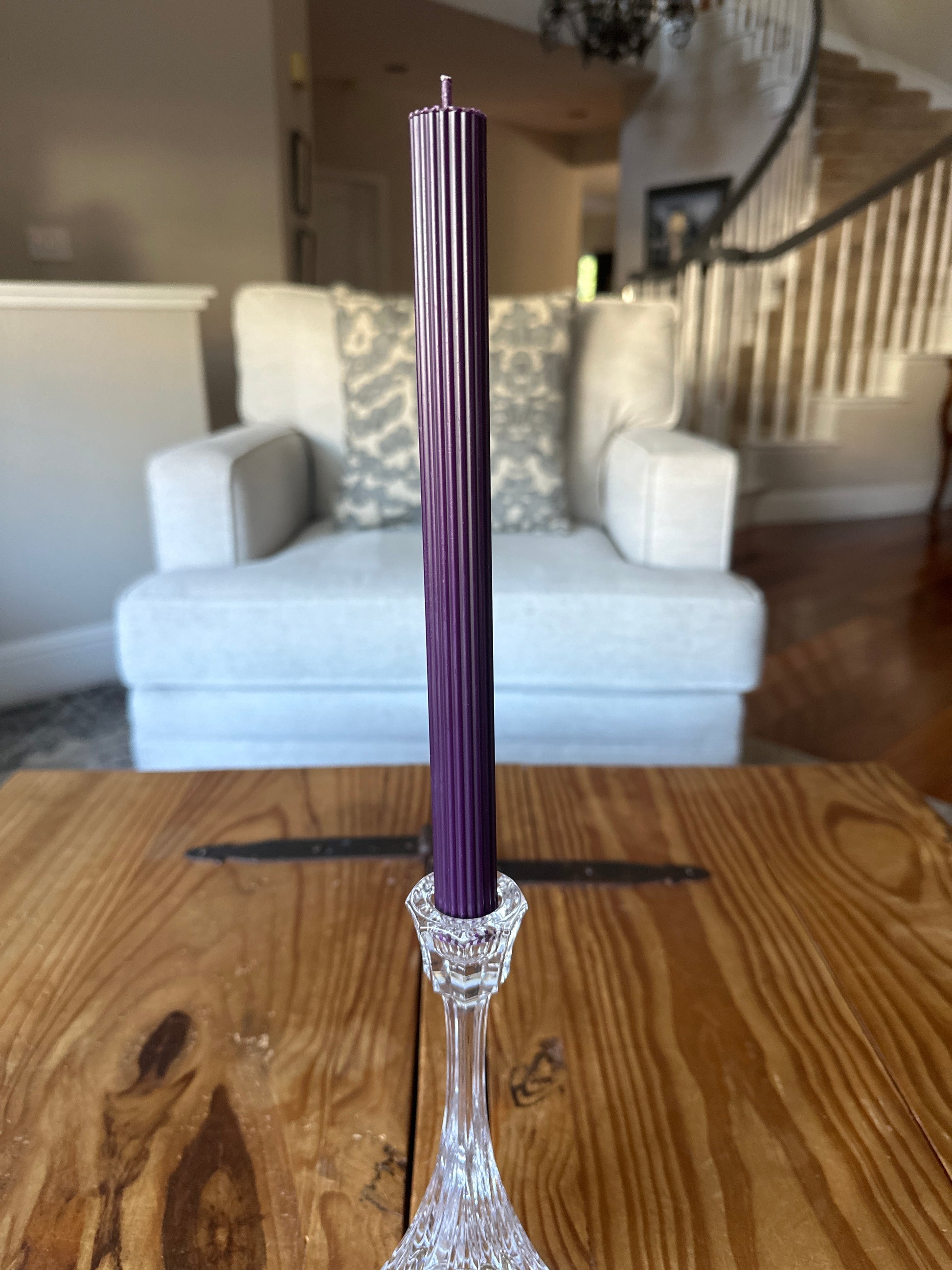 Purple ribbed taper dinner candle on rustic wooden table in a home.